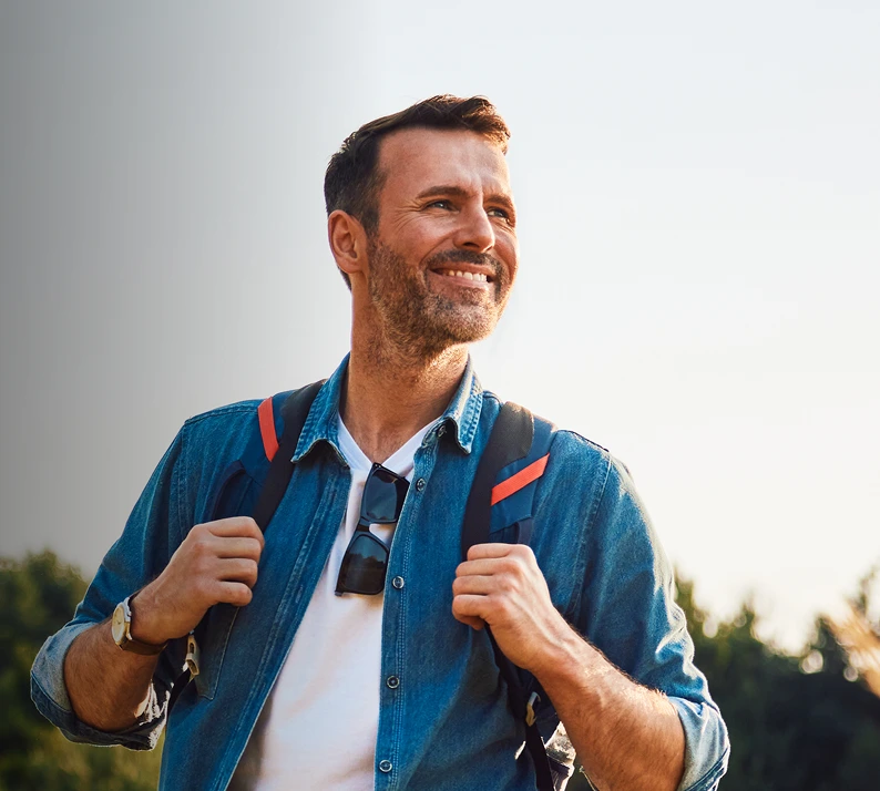 Man in blue shirt smiling outdoors with backpack straps over shoulders