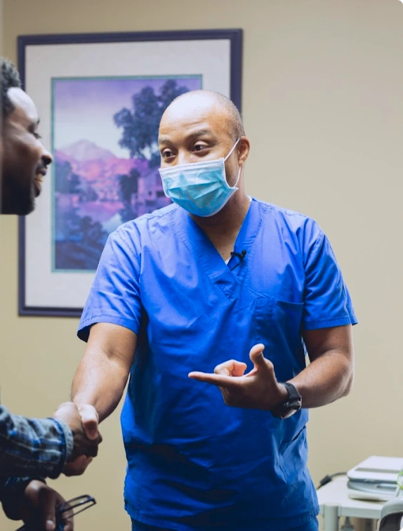 Healthcare provider in blue scrubs and mask discussing treatment with patient in clinical setting