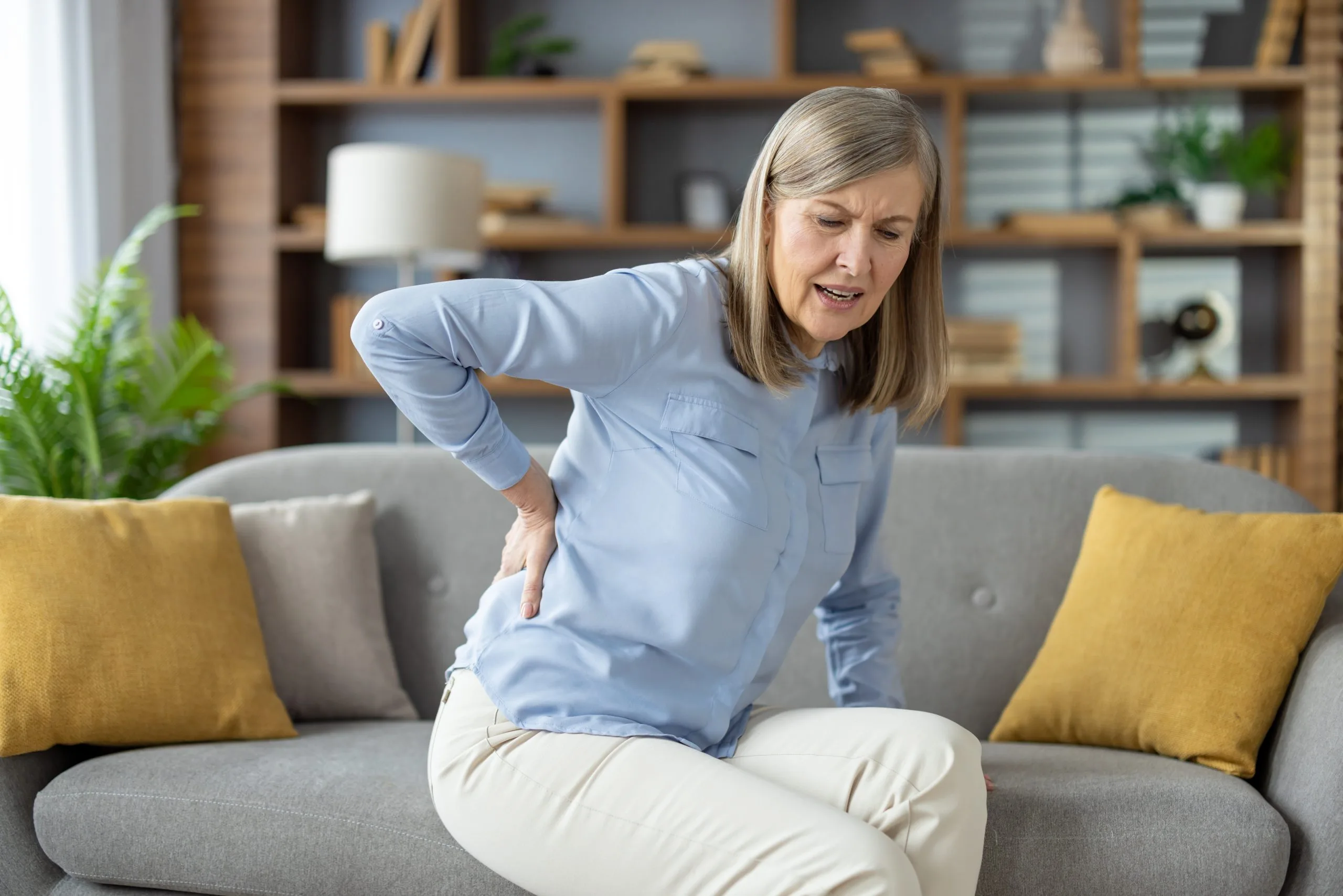 Woman on couch holding lower back in discomfort