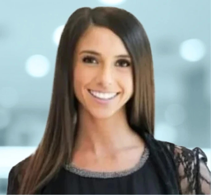 Woman with long brown hair smiling at camera against blurred office background