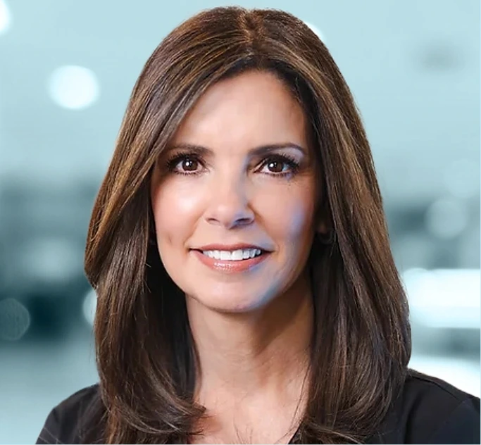 Woman with shoulder-length brown hair smiling at camera against blurred light background
