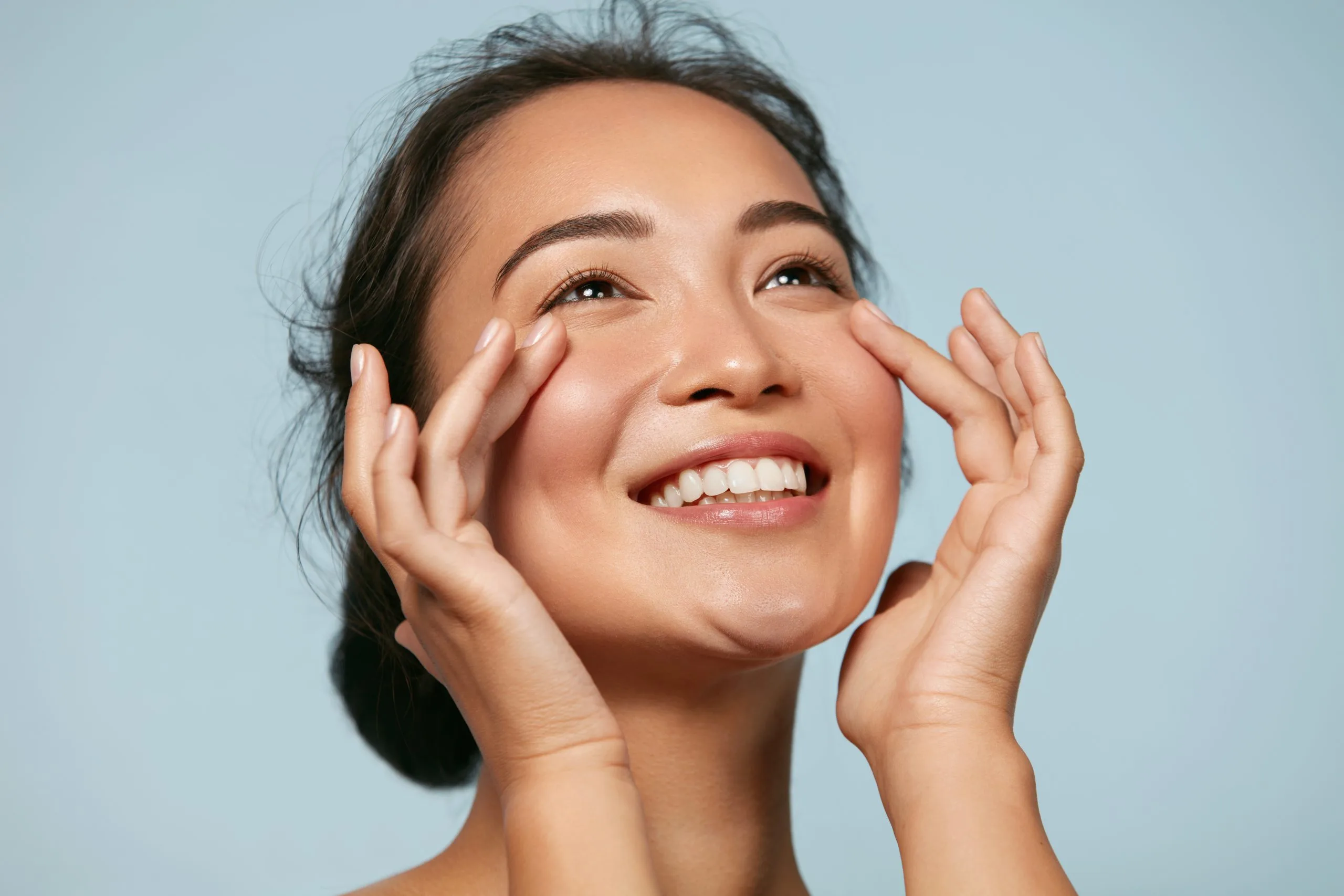 Woman with short dark hair smiling with hands near face against blue background