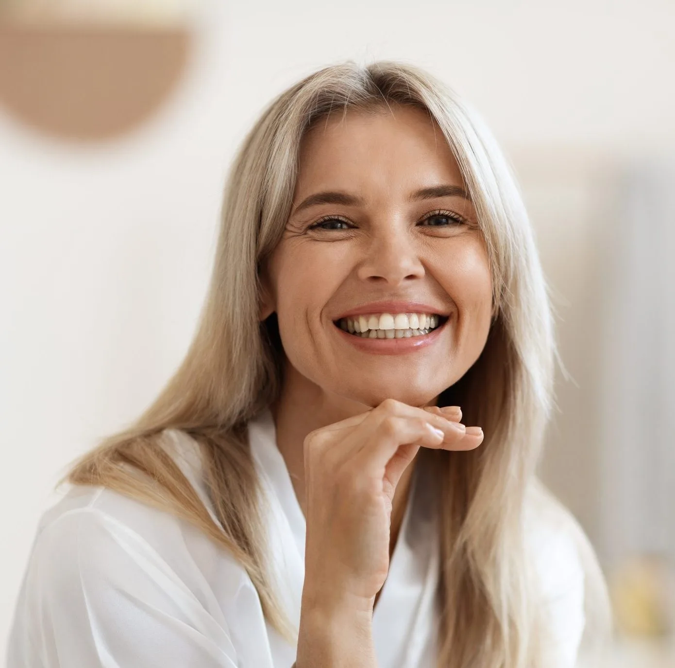 Woman with blonde hair smiling with hand near face in bright interior setting
