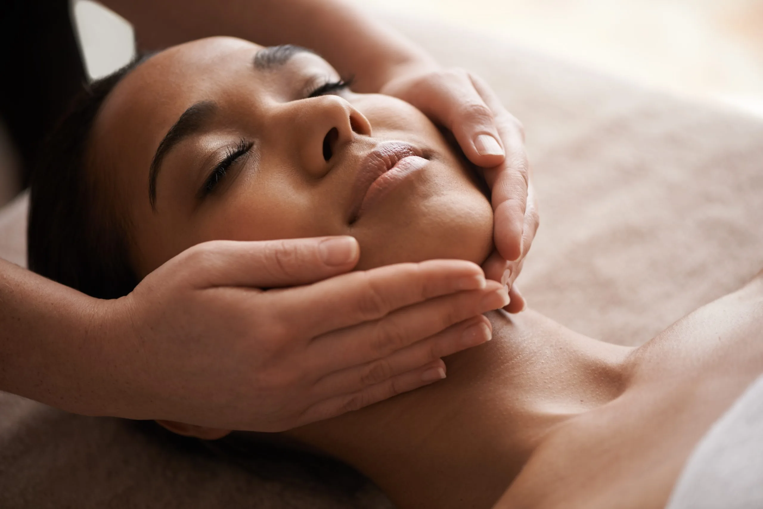 Practitioner performing facial massage on relaxed client's face and neck