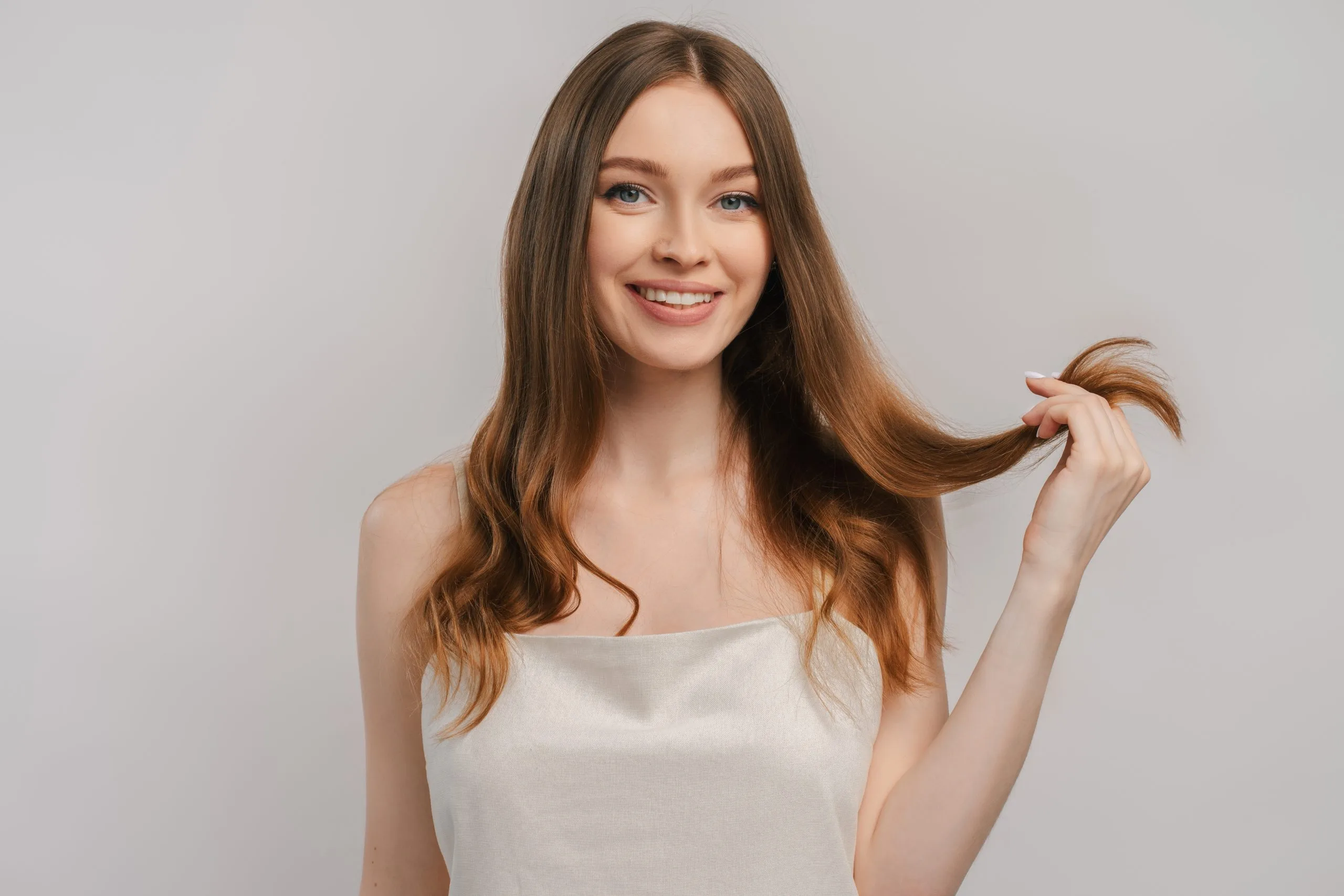 Woman with long auburn hair smiling and holding a strand of hair
