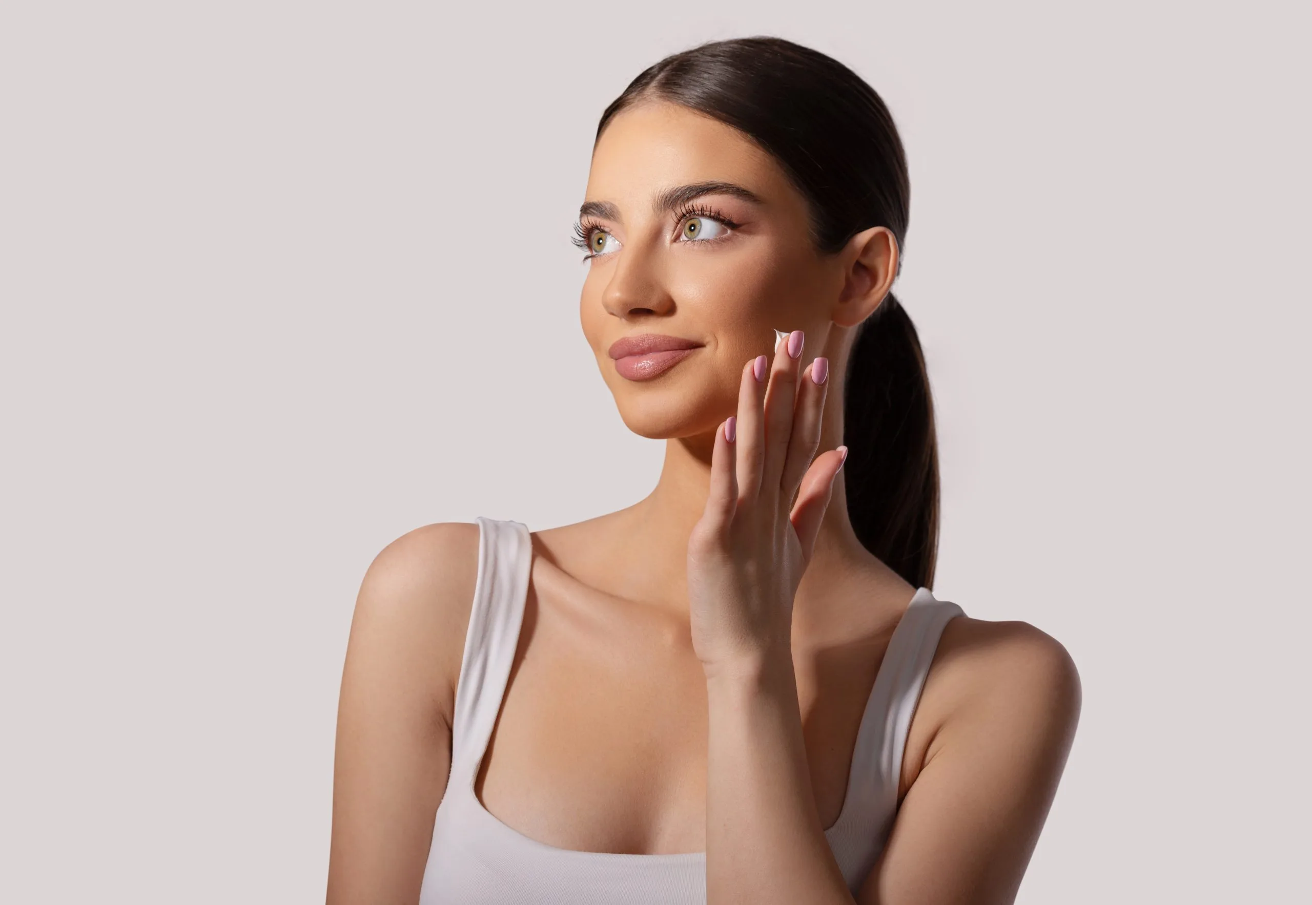 Woman with long dark hair touching her face and cheek against a gray background