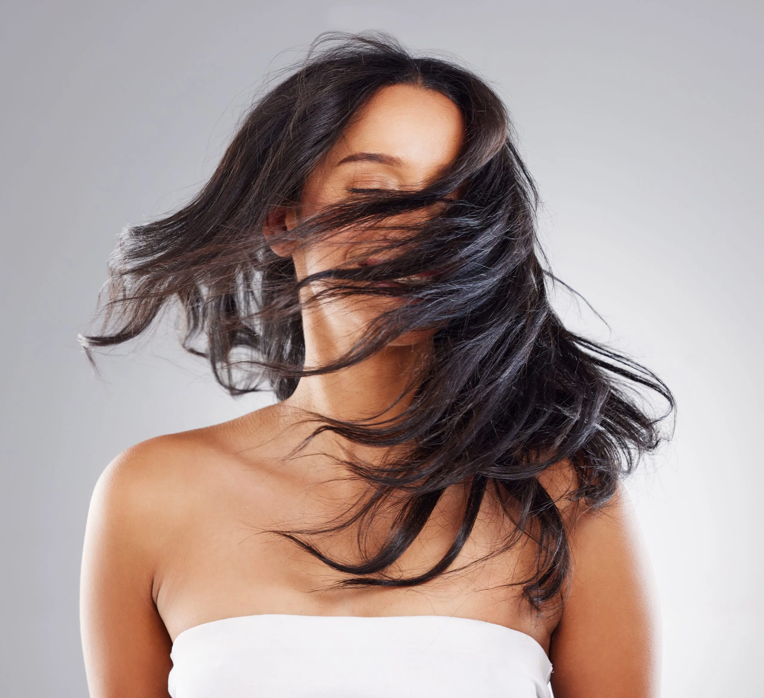 Woman with long black hair flowing across her face and shoulder against a gray background