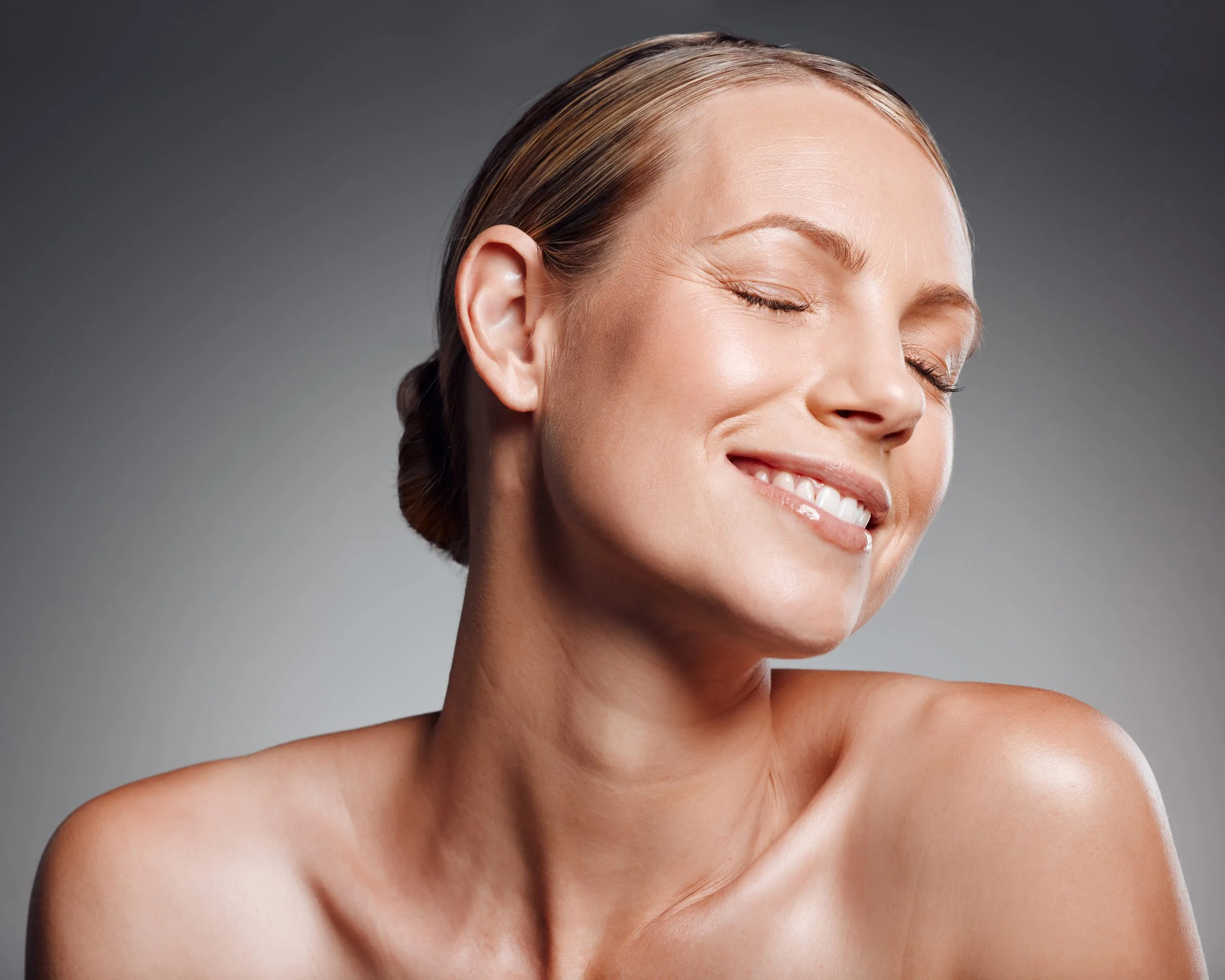 Woman with eyes closed, smiling with head tilted, showing clear glowing skin
