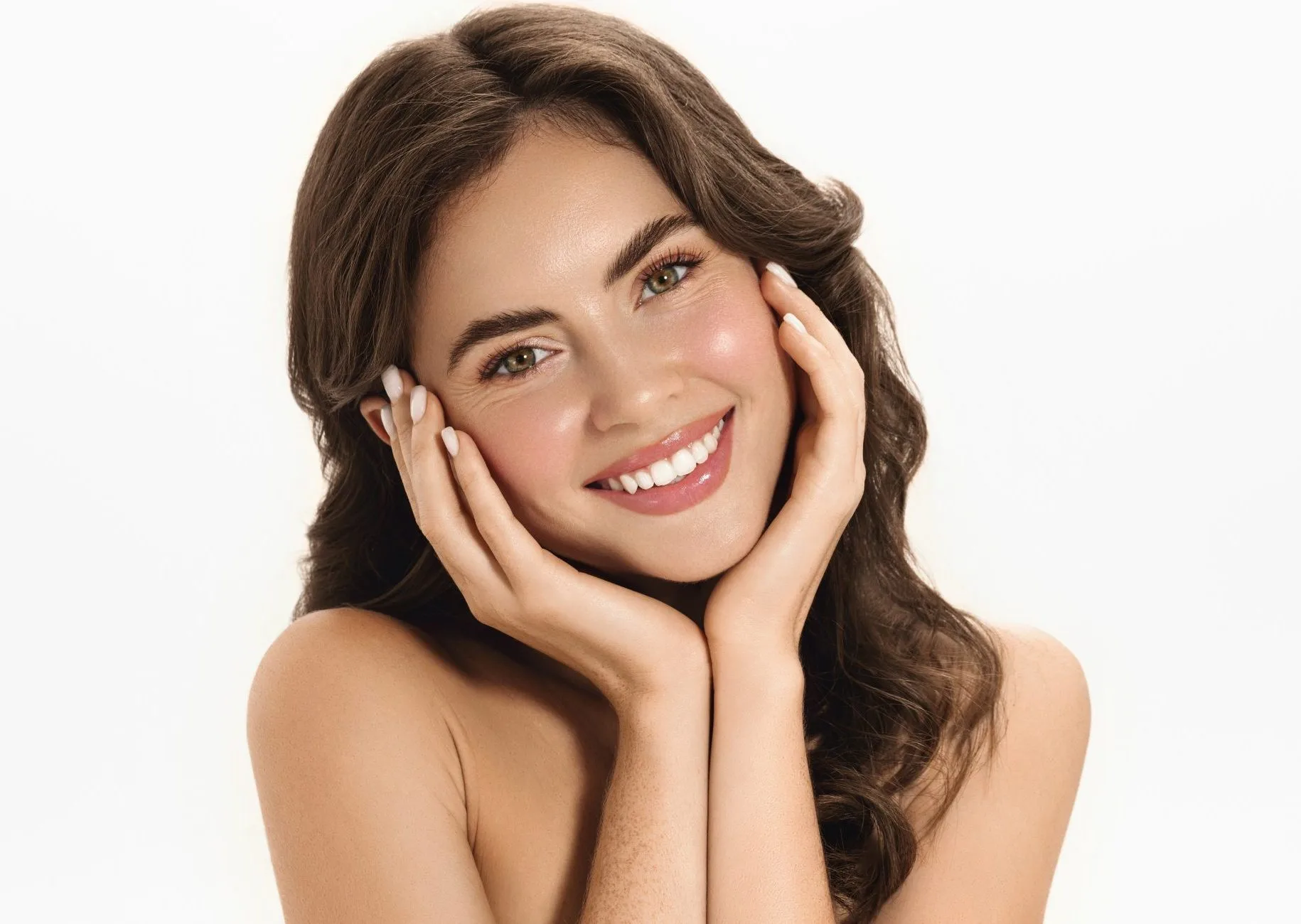 Woman with wavy hair cradling her face with both hands, smiling