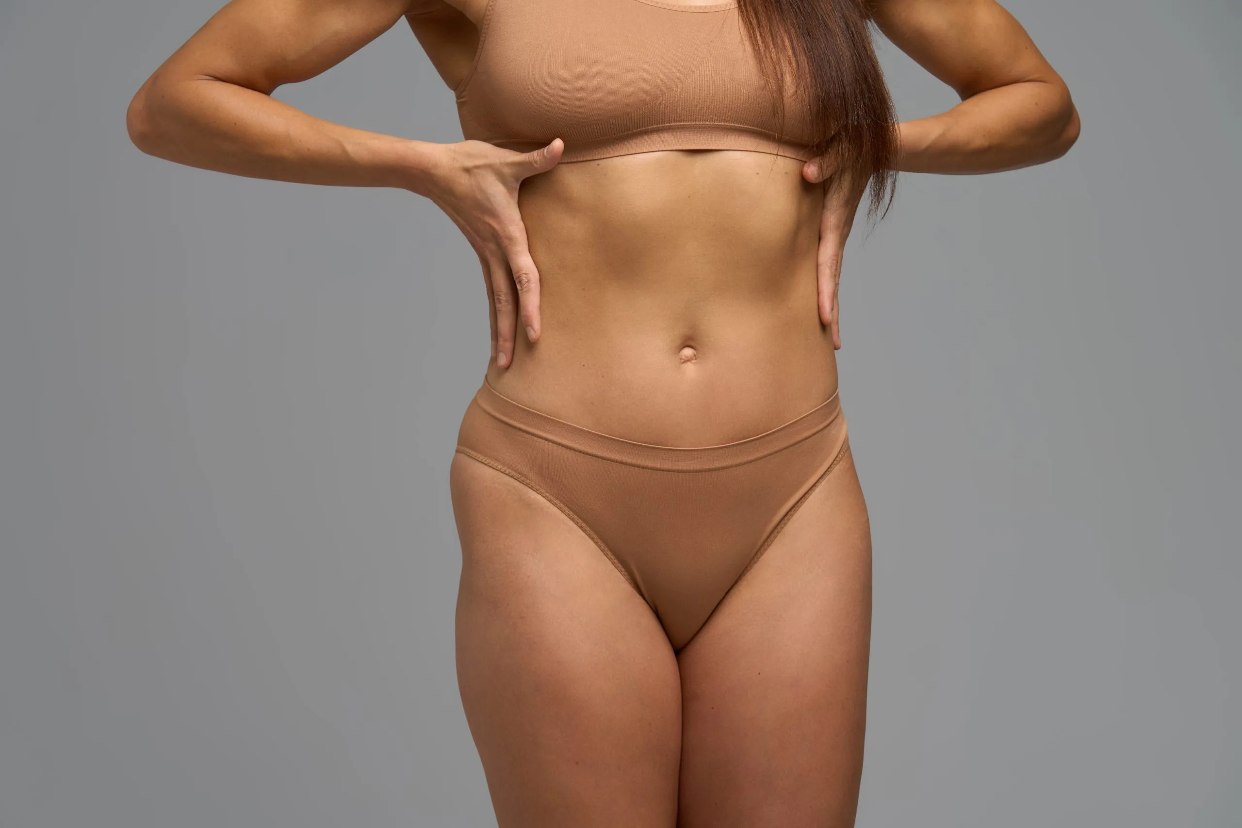 Woman showing abdominal definition by lifting beige crop top