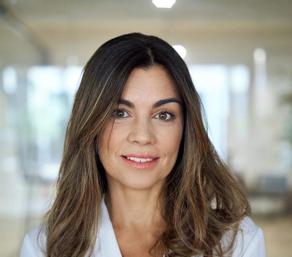 Woman with dark hair and neutral expression in modern medical office hallway