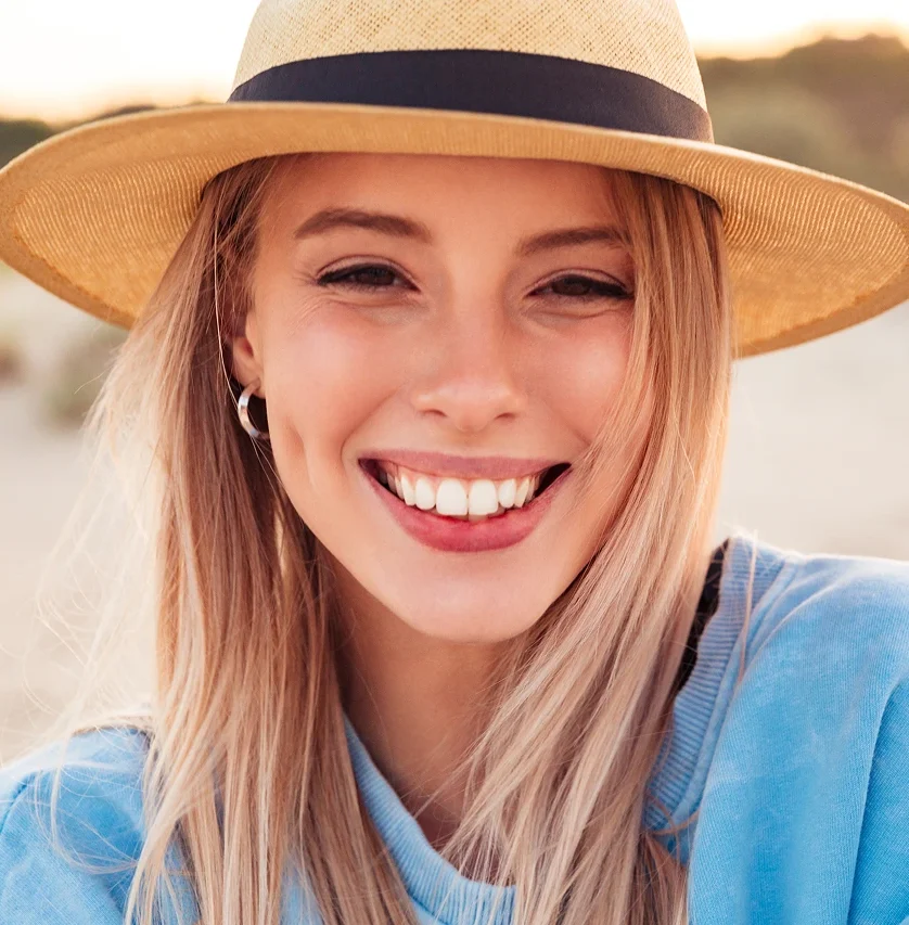 Smiling woman wearing straw hat and blue shirt outdoors in natural setting