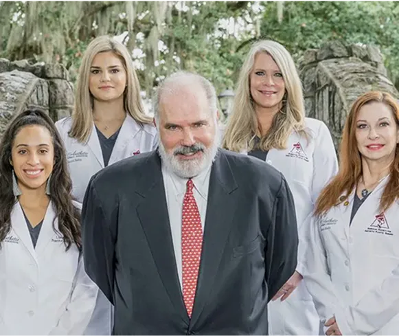 Medical team of five professionals in white coats with male doctor in center wearing dark suit and red tie