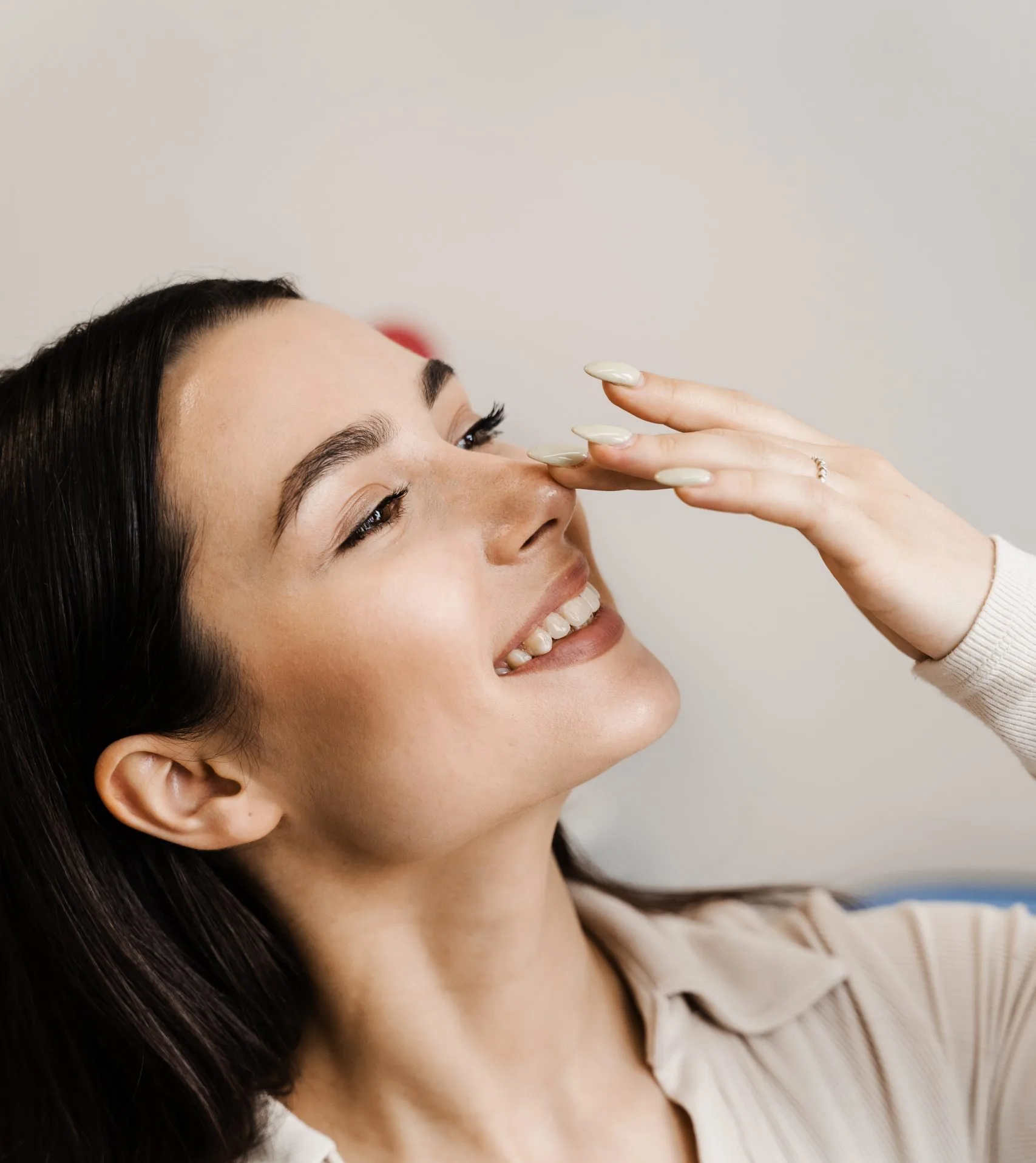 Woman touching her nose and smiling, displaying clear skin