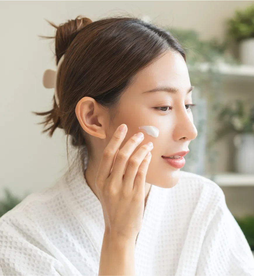 Woman applying skincare product to her cheek indoors near a window