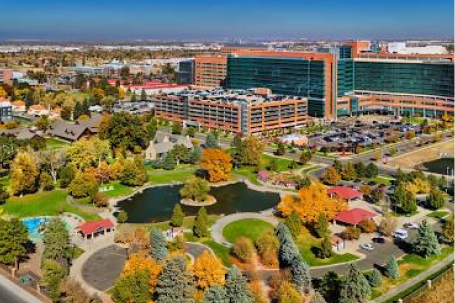 Aerial view of Aurora, Colorado showing modern office buildings, green landscaping, and a pond with fall foliage