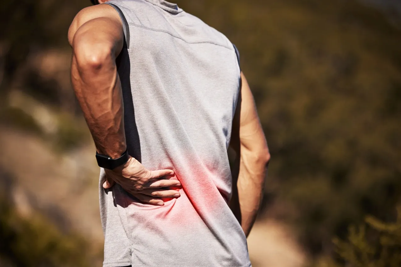 A man outdoors grips his lower back in pain, highlighted with a red graphic overlay indicating discomfort.