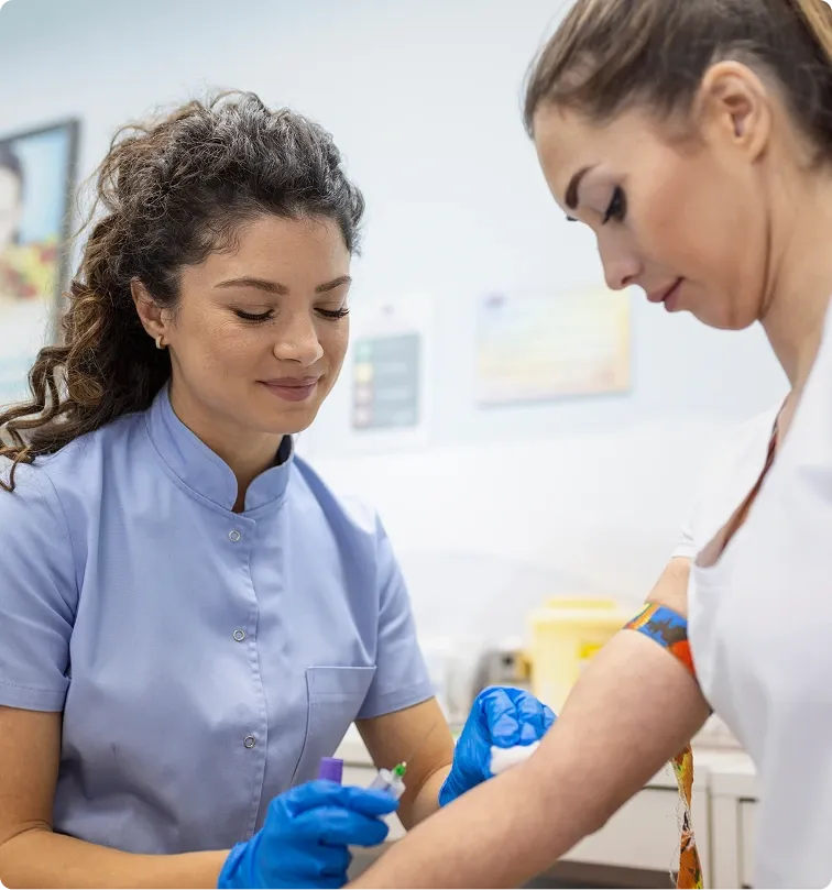 A nurse in blue scrubs draws blood from a patient's arm in a clinical office setting.