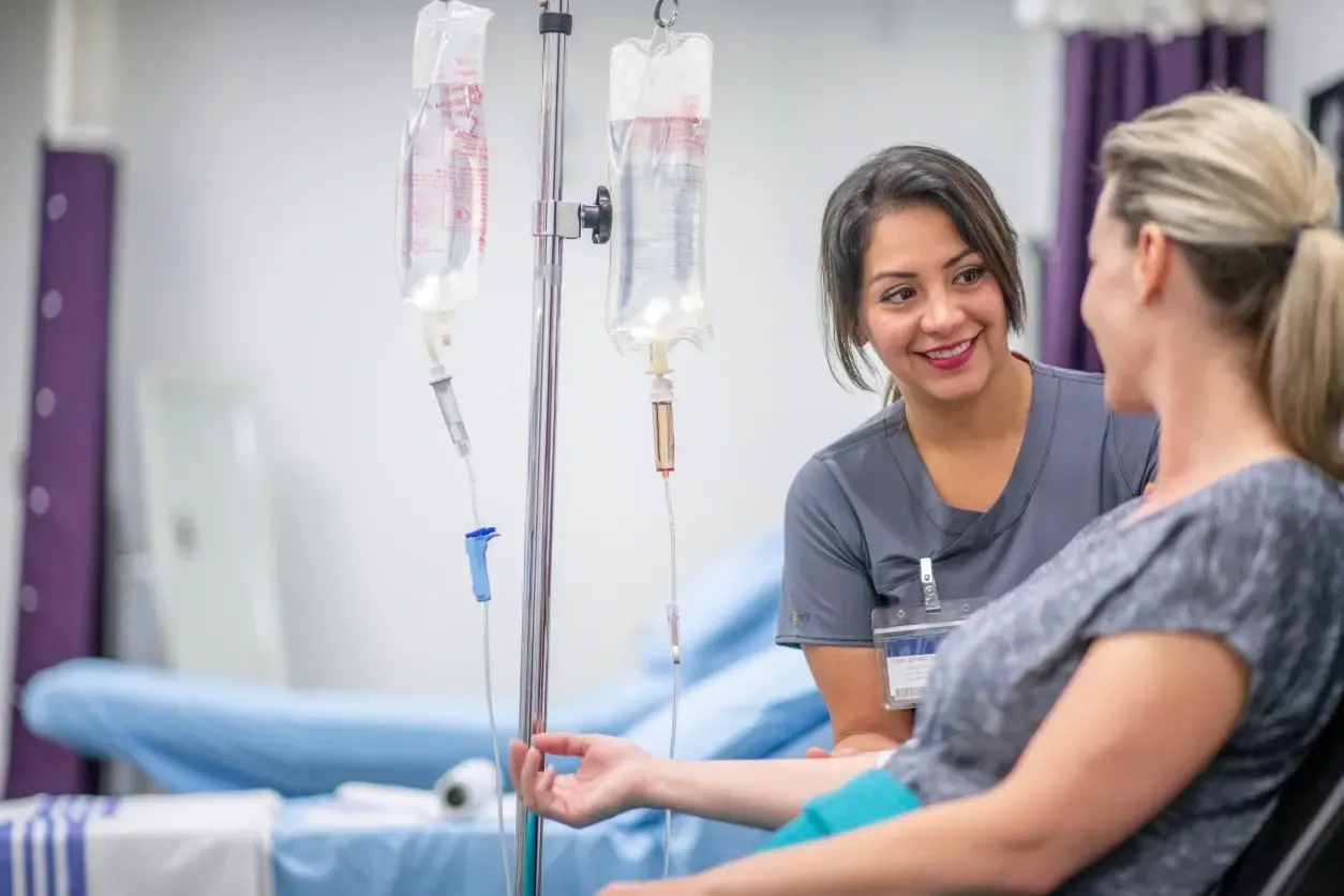 A smiling nurse talks with a seated patient receiving IV hydration therapy in a medspa treatment room.
