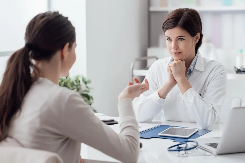 Stock photo of a female doctor in a white coat listening attentively to a patient during a consultation, used to illustrate a blog post about ketamine treatment.