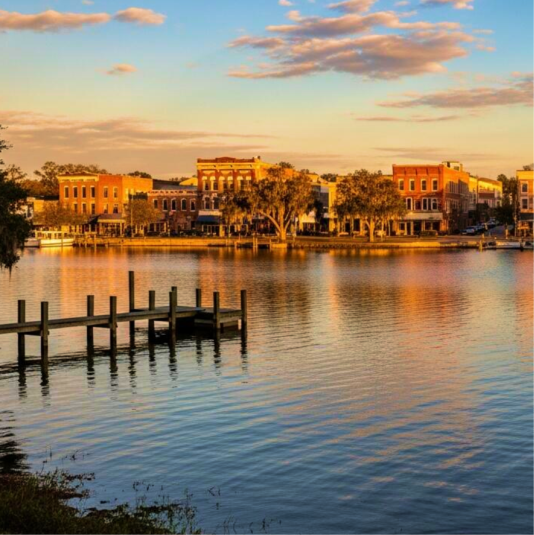 Waterfront sunset view of historic orange and red brick buildings reflected in calm water with wooden dock in foreground