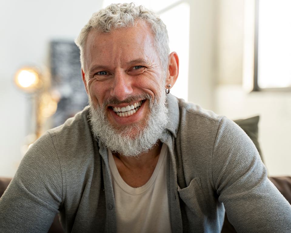 Smiling older man with gray beard wearing olive cardigan indoors