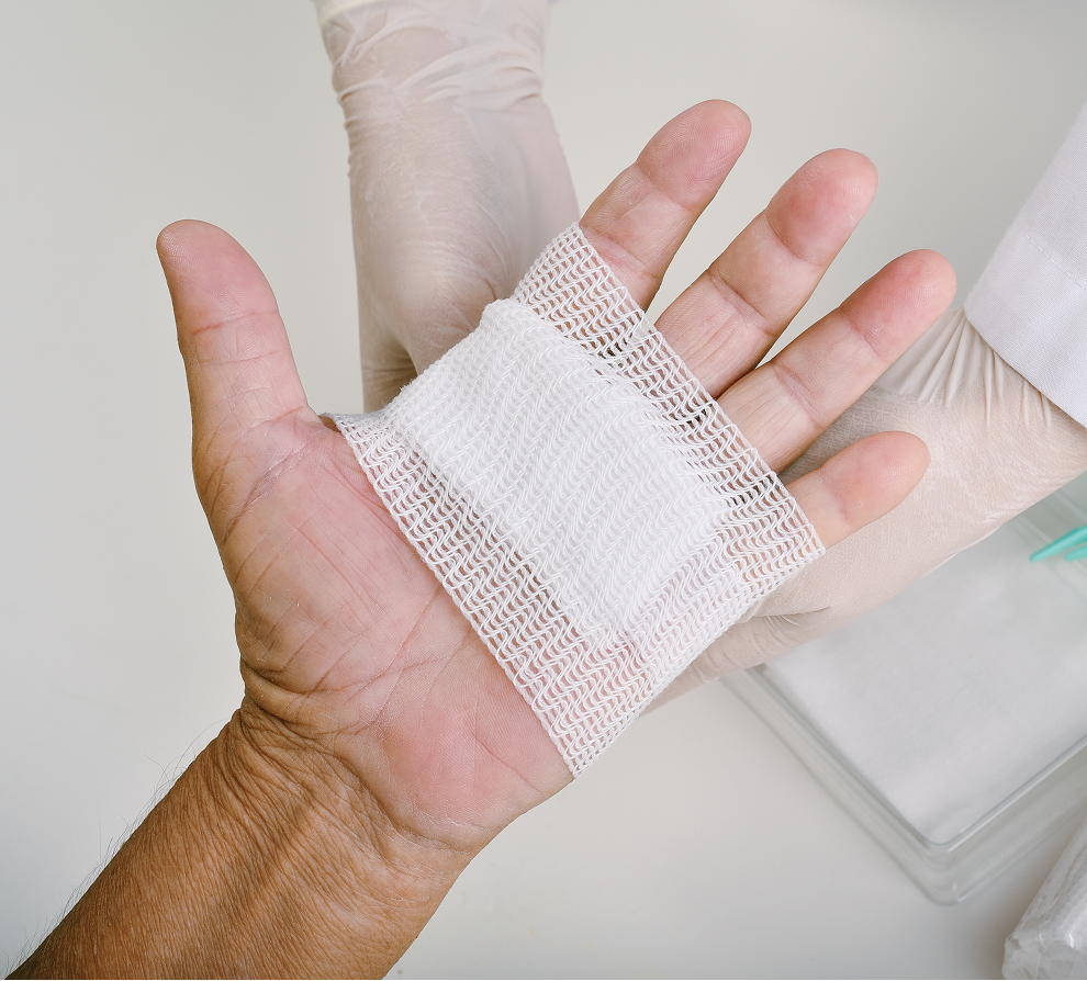 Healthcare worker's gloved hands holding white gauze pad on patient's hand