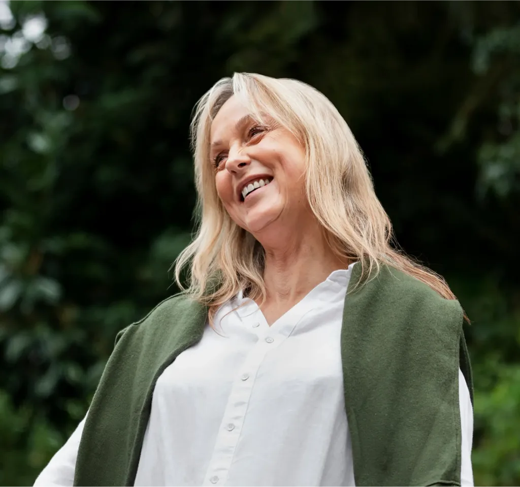 Smiling woman with blonde hair wearing white shirt and green cardigan outdoors