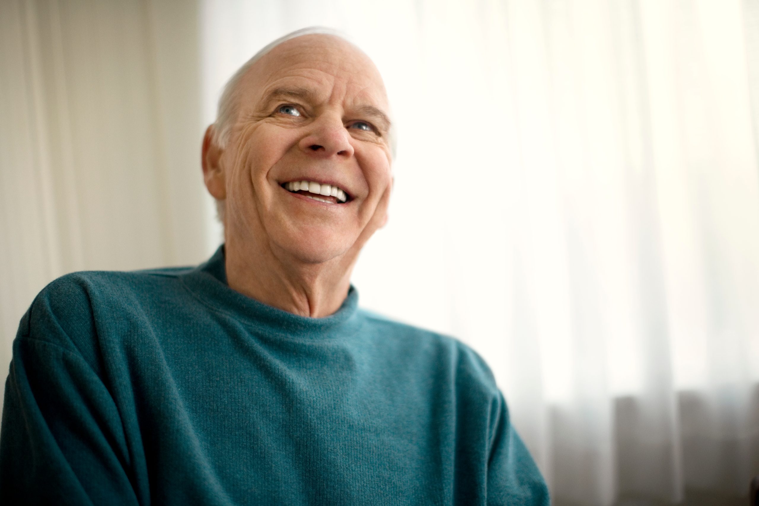 Senior man smiling indoors wearing teal shirt