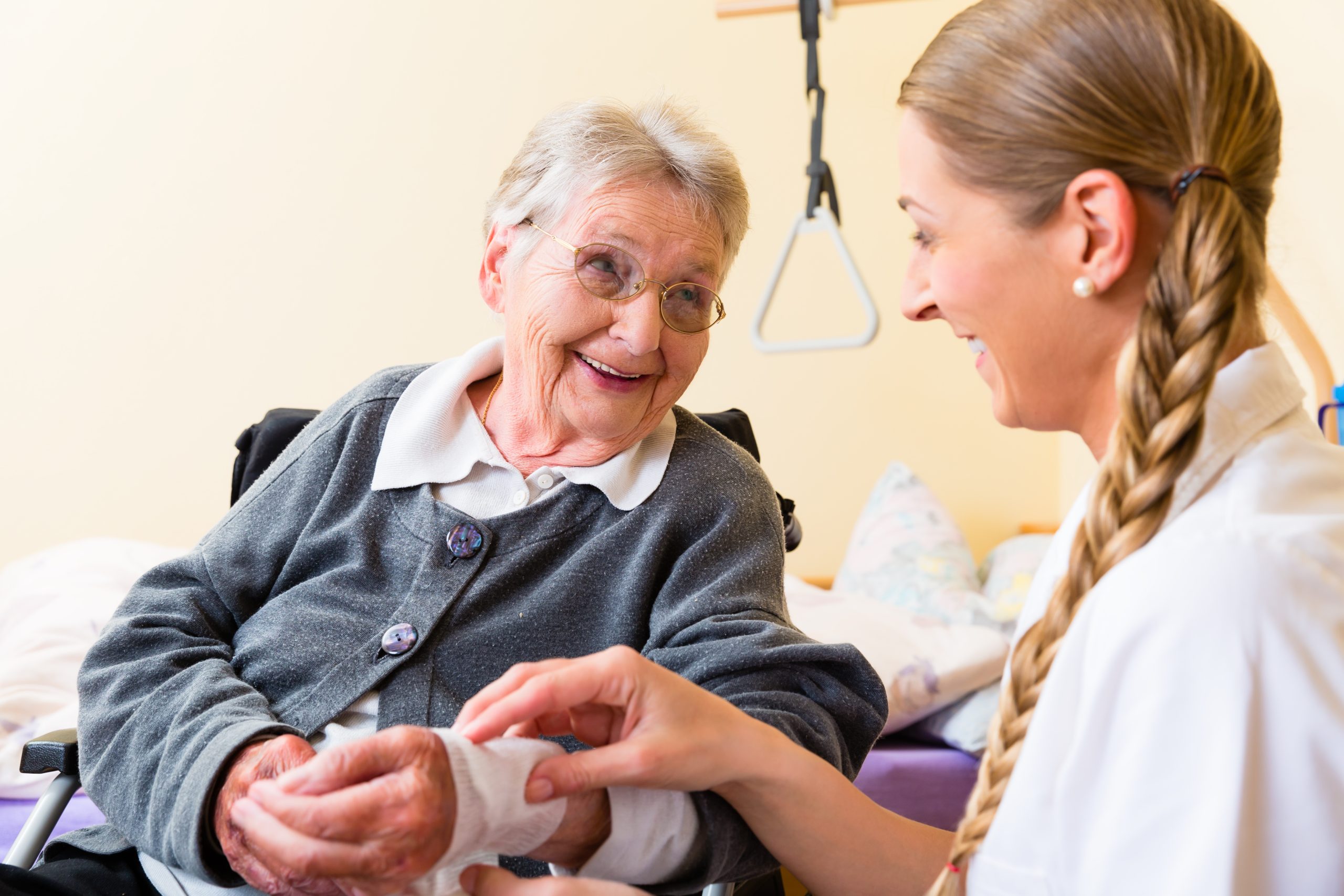 Nurse bandaging senior woman's hand while she smiles during wound care treatment