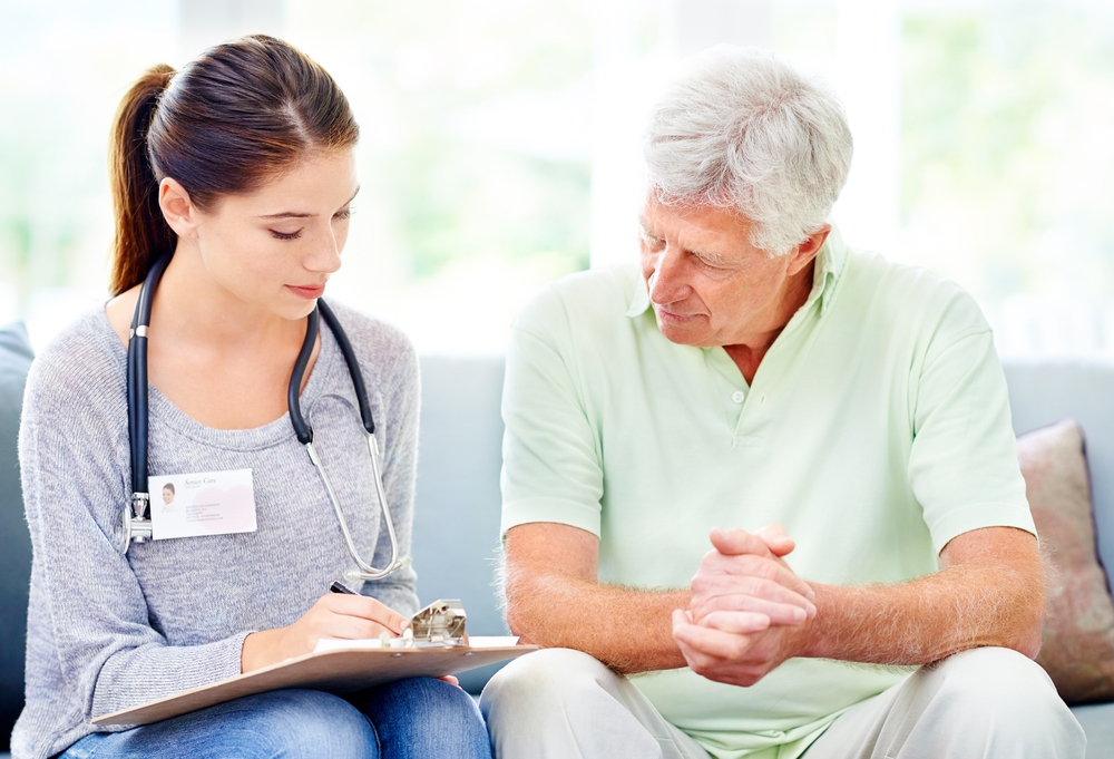 Doctor reviewing consultation notes with senior man during home visit