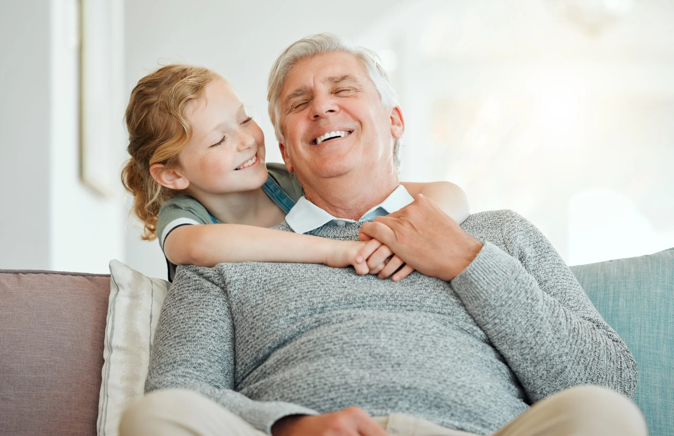 Older man and young girl hugging on a couch, both smiling