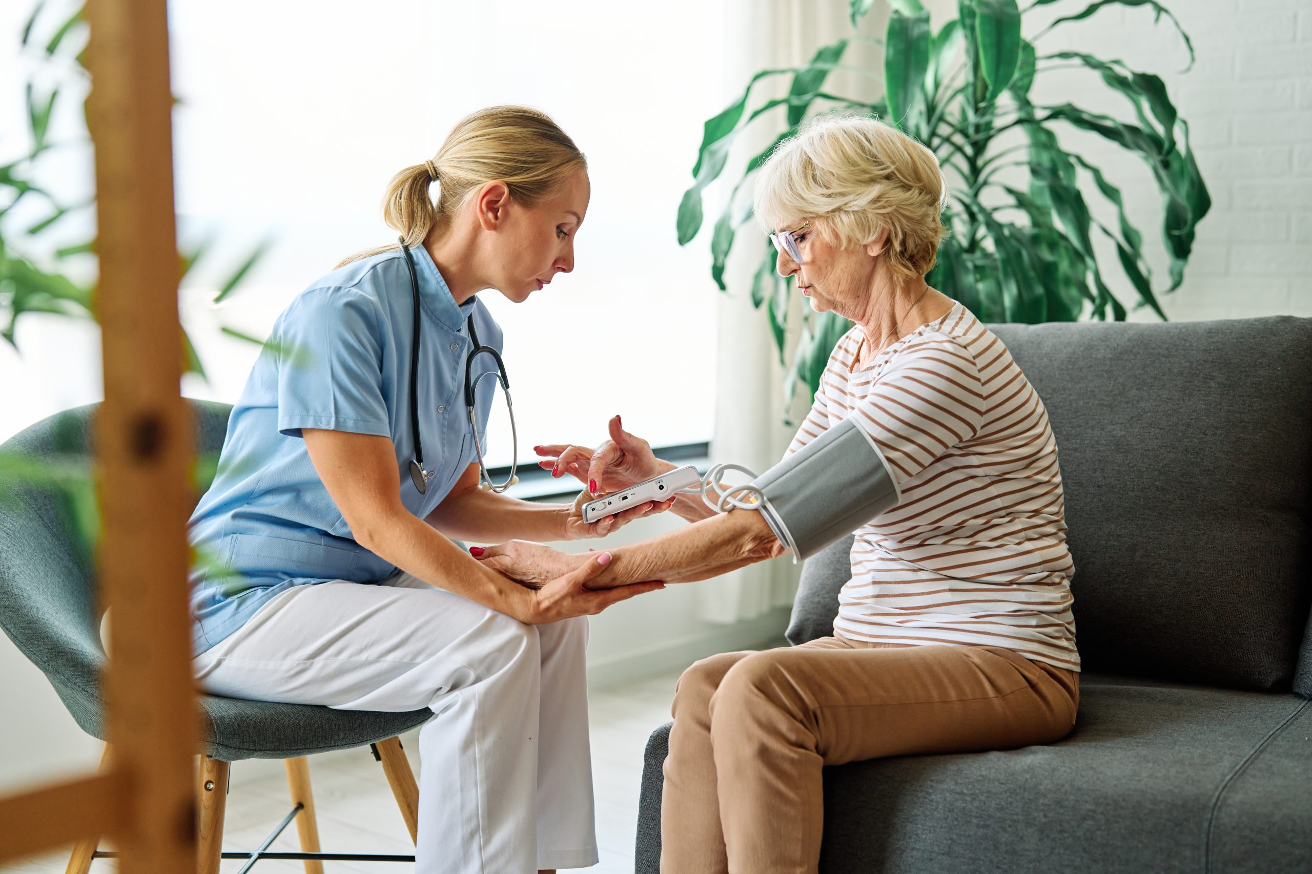 Nurse taking blood pressure reading from senior woman on couch