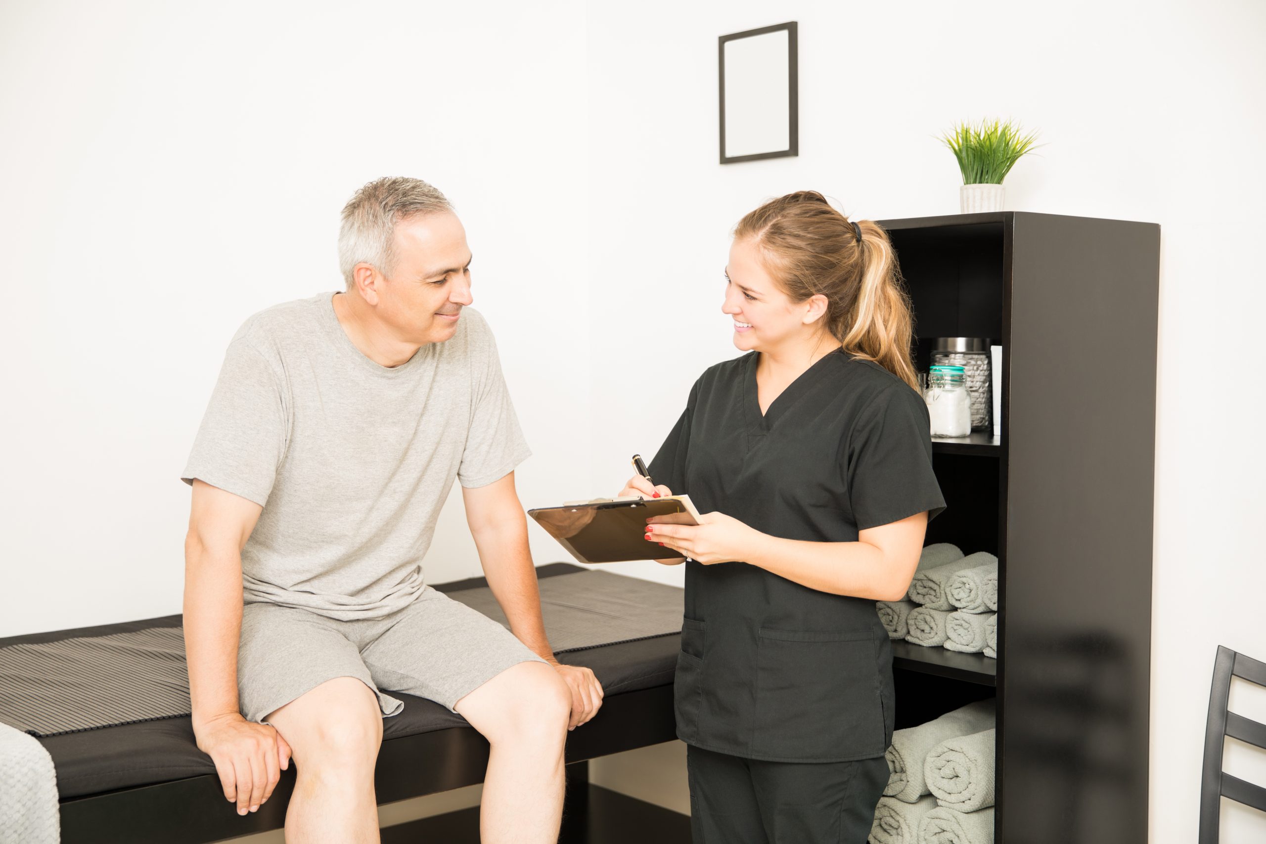 Physiotherapist writing on clipboard while consulting with male patient in clinical setting