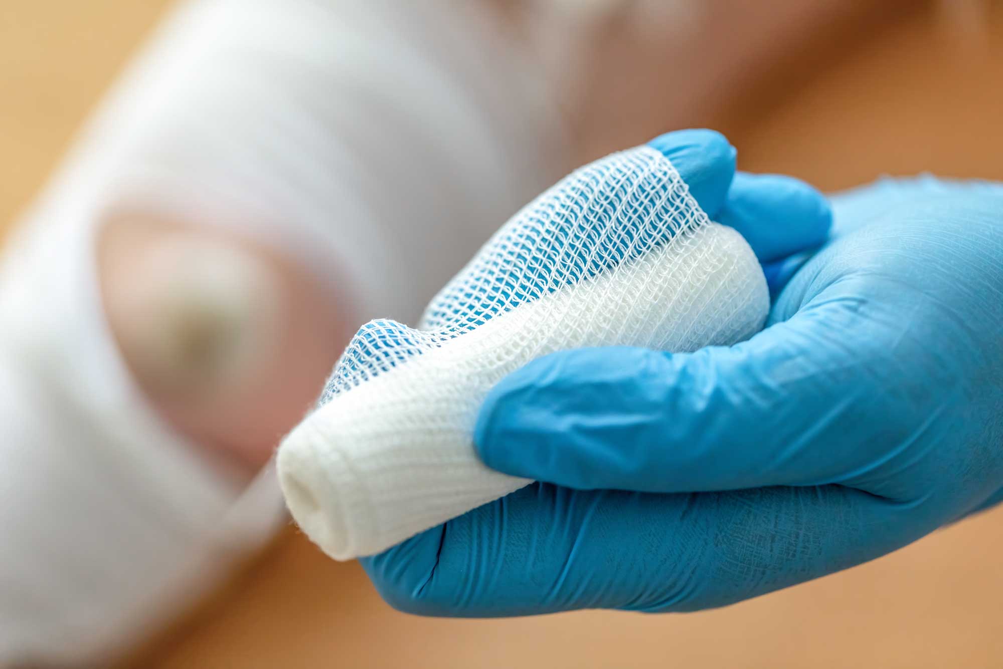 Gloved hand holding sterile white wound dressing with blue mesh backing