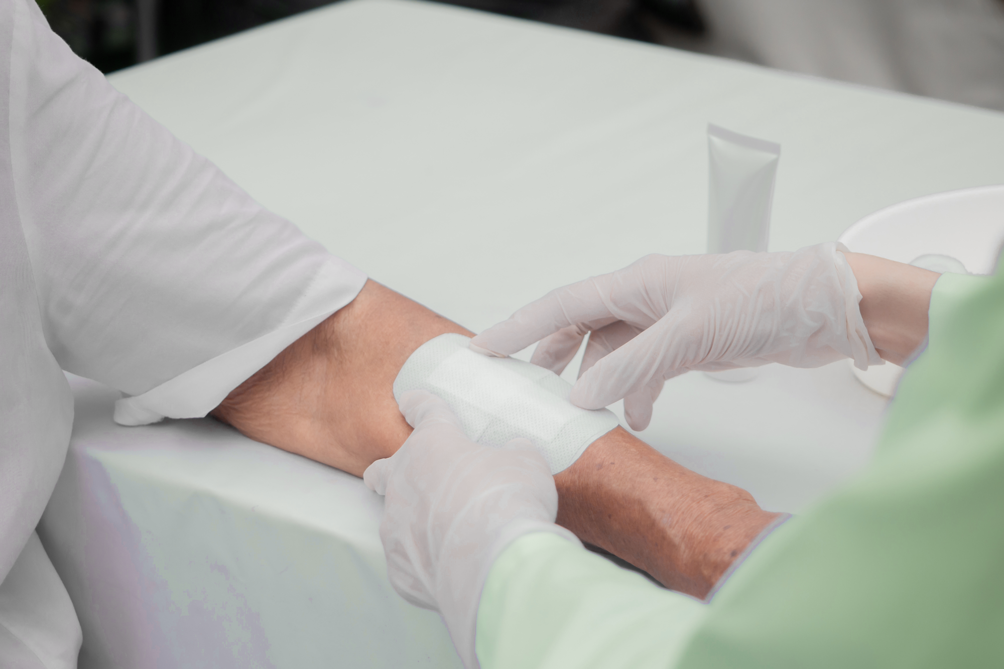 Healthcare provider applying white gauze bandage to patient's wrist at table