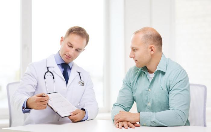 Doctor with stethoscope writing notes while consulting with male patient