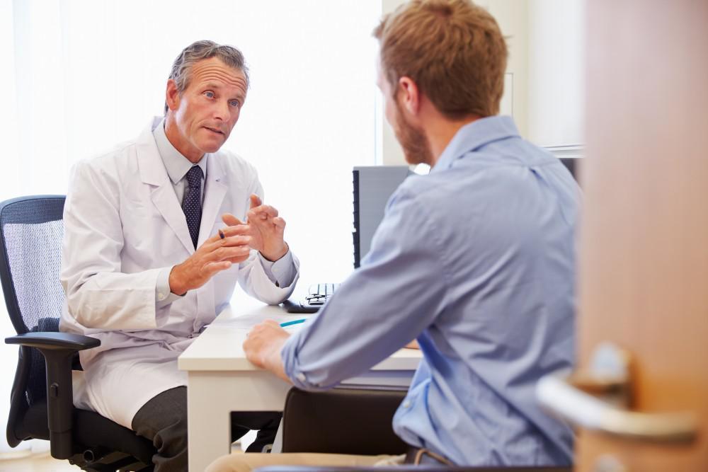Psychiatrist in white coat discussing treatment with male patient at office desk