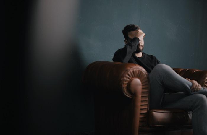 Man sitting on leather chair looking troubled, experiencing mental distress