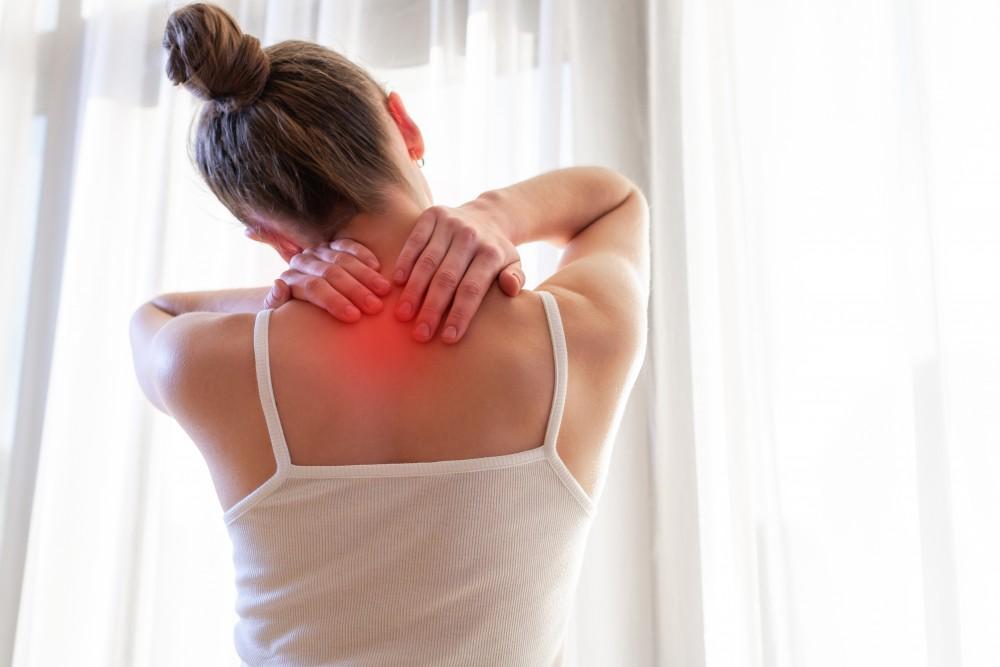 Woman from behind holding her neck and shoulder with red highlight indicating pain