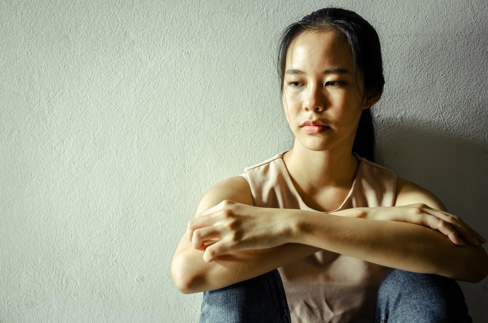 Young woman with arms crossed looking downward with a serious expression