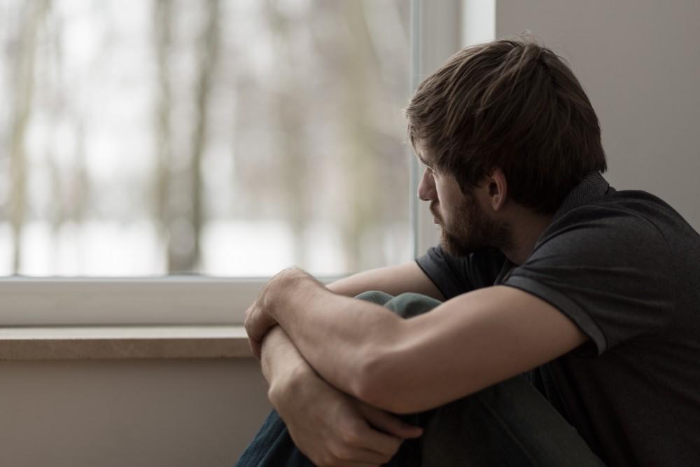 Man sitting by window looking outside, head bowed in contemplative pose