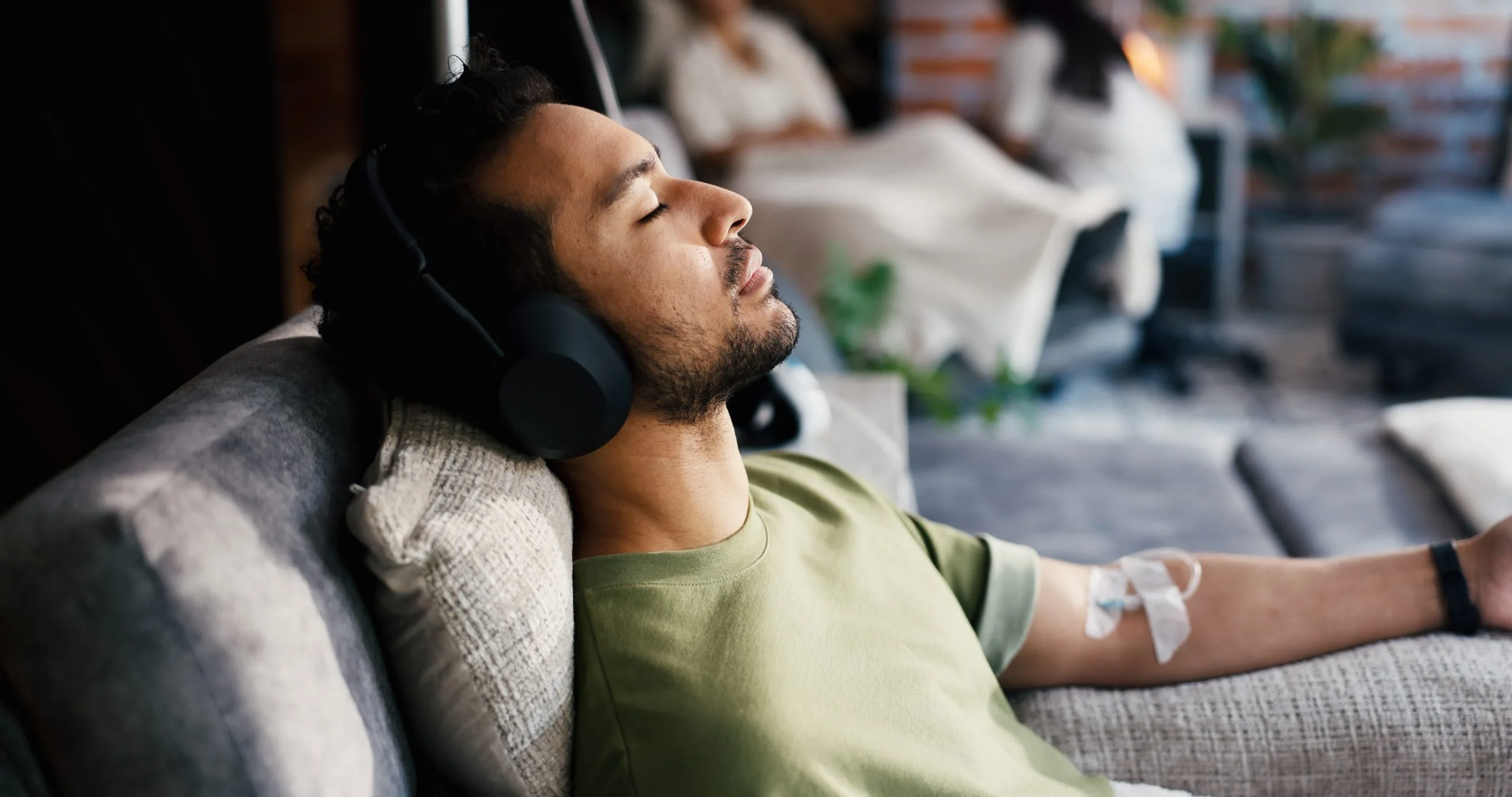 Man resting on a sofa with headphones on during an IV infusion