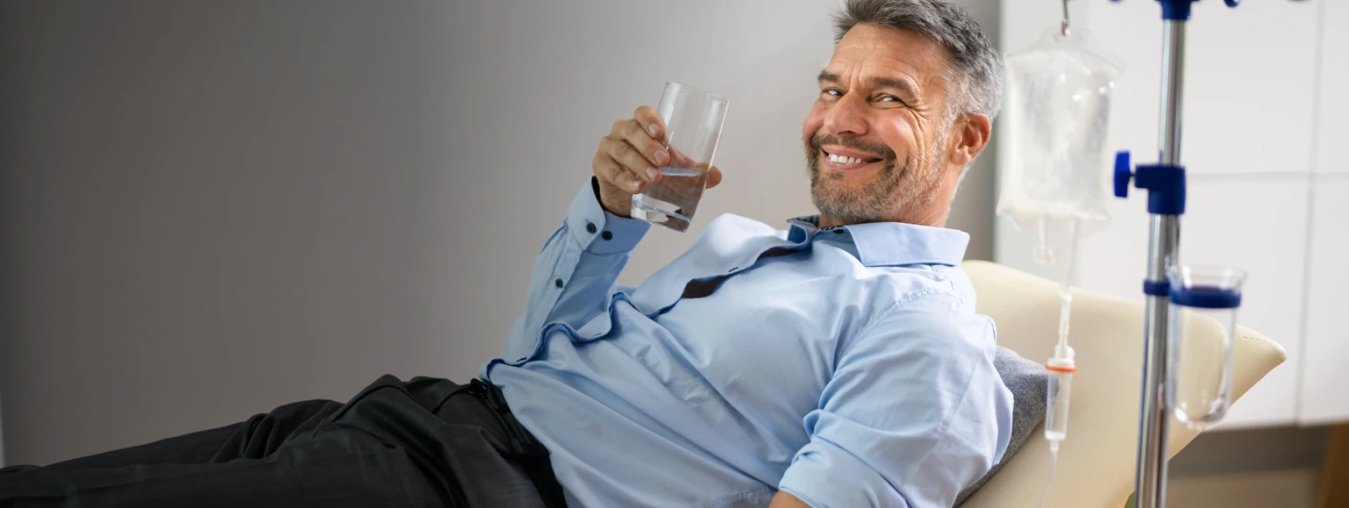 Smiling man holding a glass of water while receiving an IV infusion