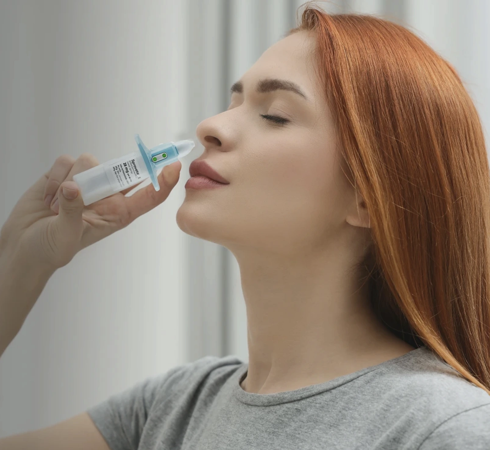 Woman with eyes closed using a nasal spray device