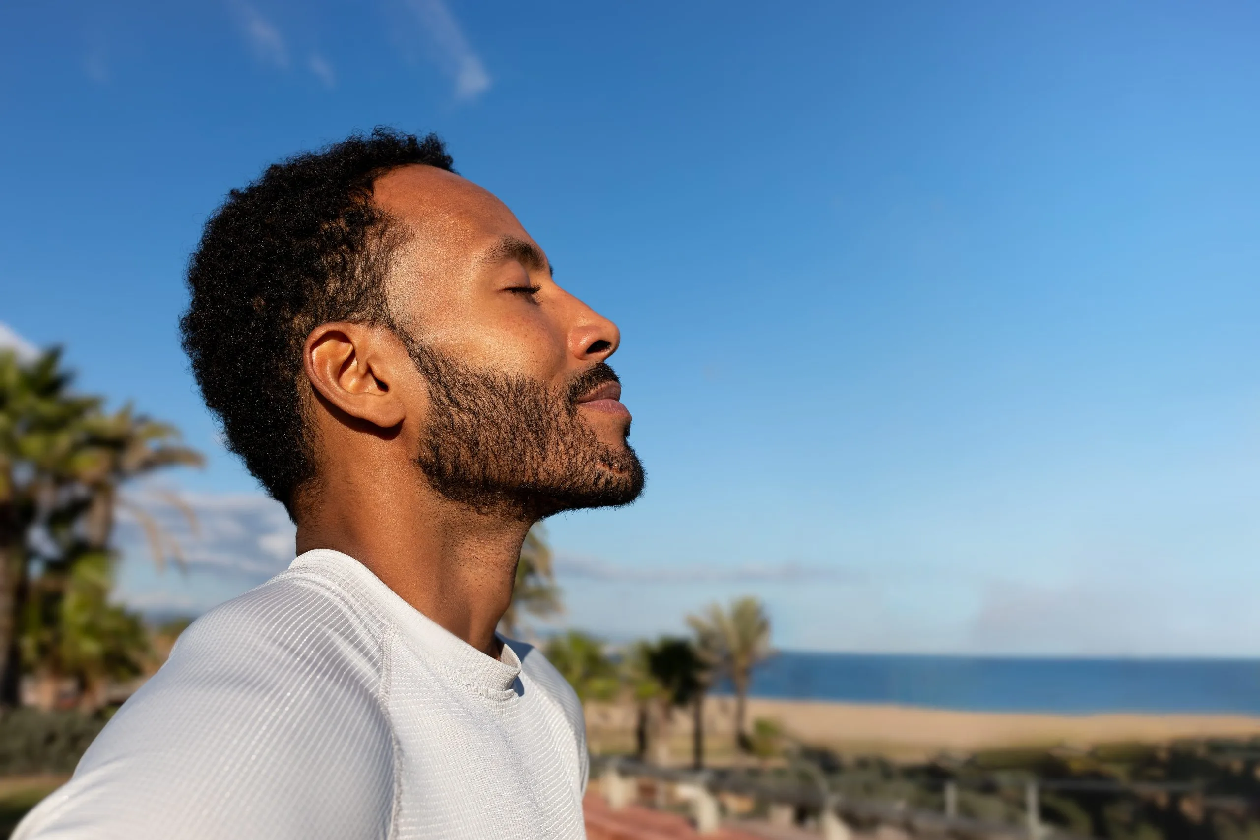 Man breathing deeply outdoors with palm trees and the ocean behind him