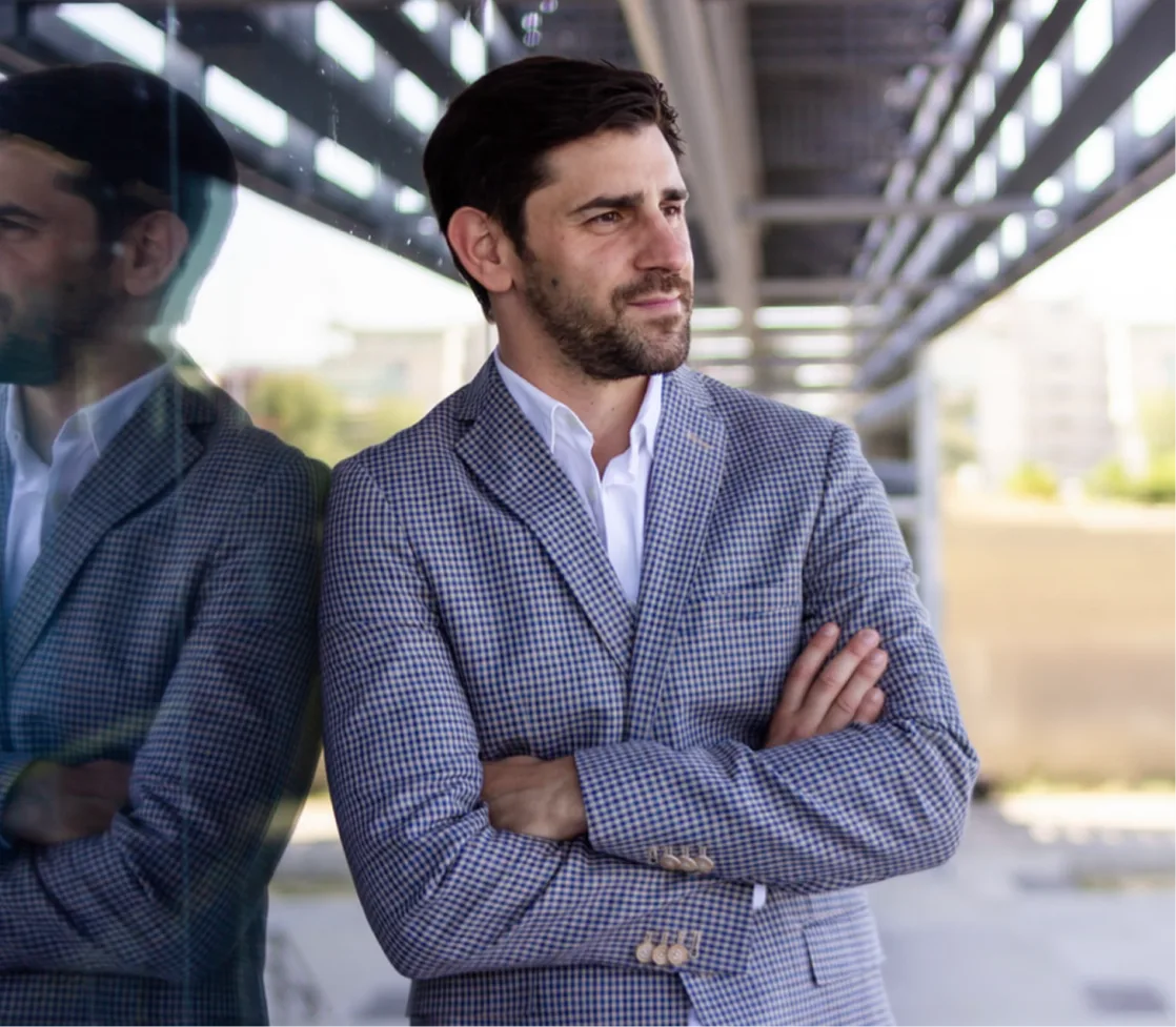 Man in checkered blazer standing with arms crossed in modern building with glass reflection