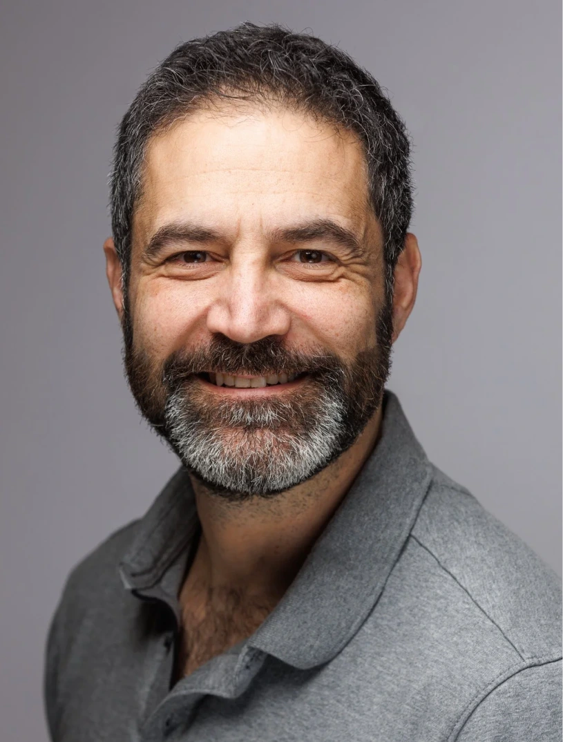Middle-aged man with beard in gray collared shirt, smiling at camera