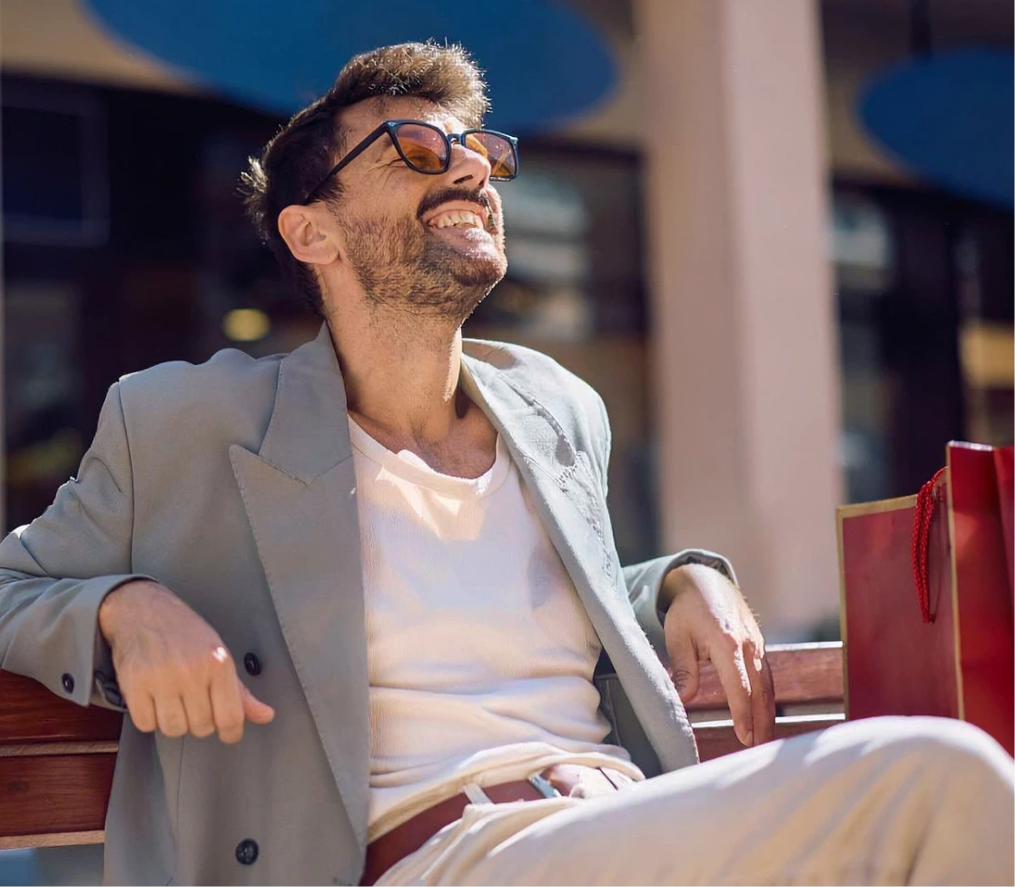 Man wearing glasses and blazer smiling while sitting outdoors in sunlight