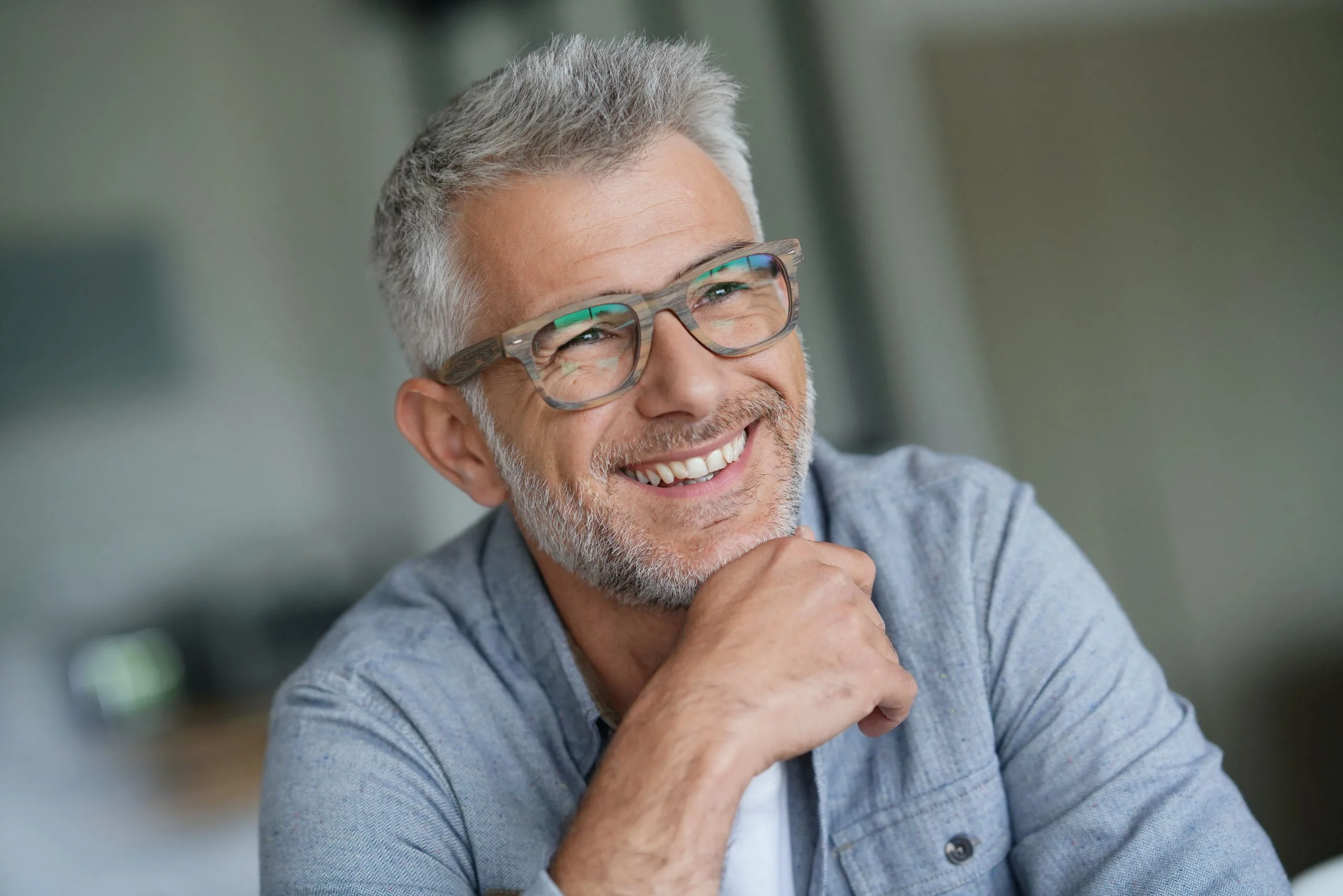 Smiling man with gray hair and glasses wearing a light blue shirt